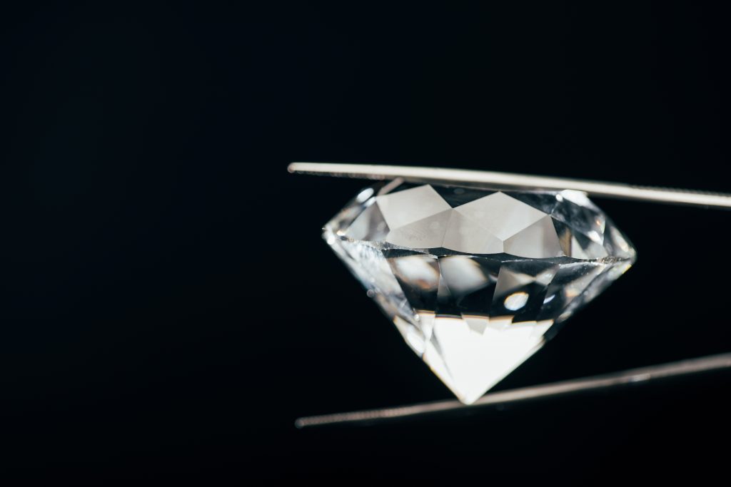 Diamond held from the side with tweezers against a black background