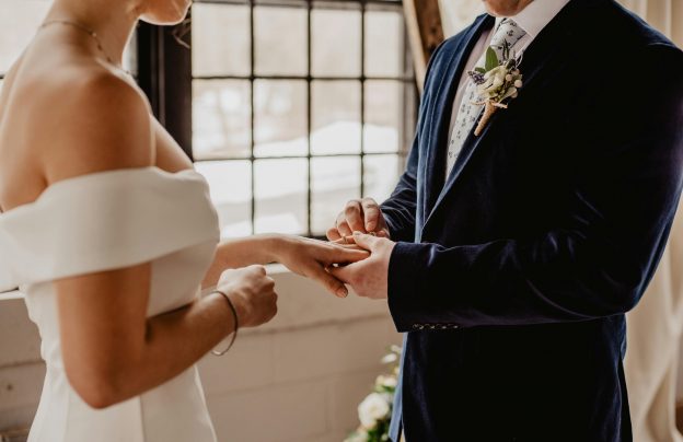 Bräutigam steckt der Braut den Ring an, symbolisiert Trauung und Liebe.