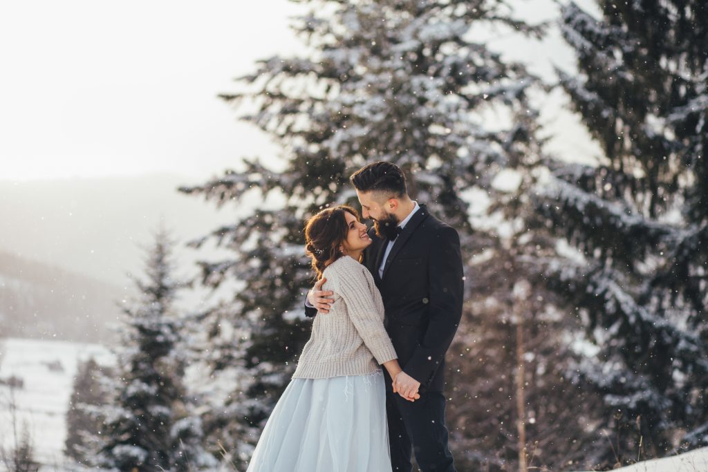 Brautpaar auf dem Berg zwischen verschneiten Bäumen im Hochzeitskleid und Anzug