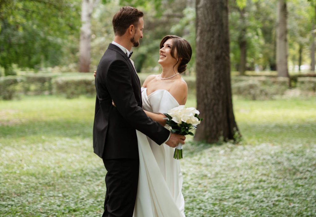 Bride and groom in wedding attire laughing in the park