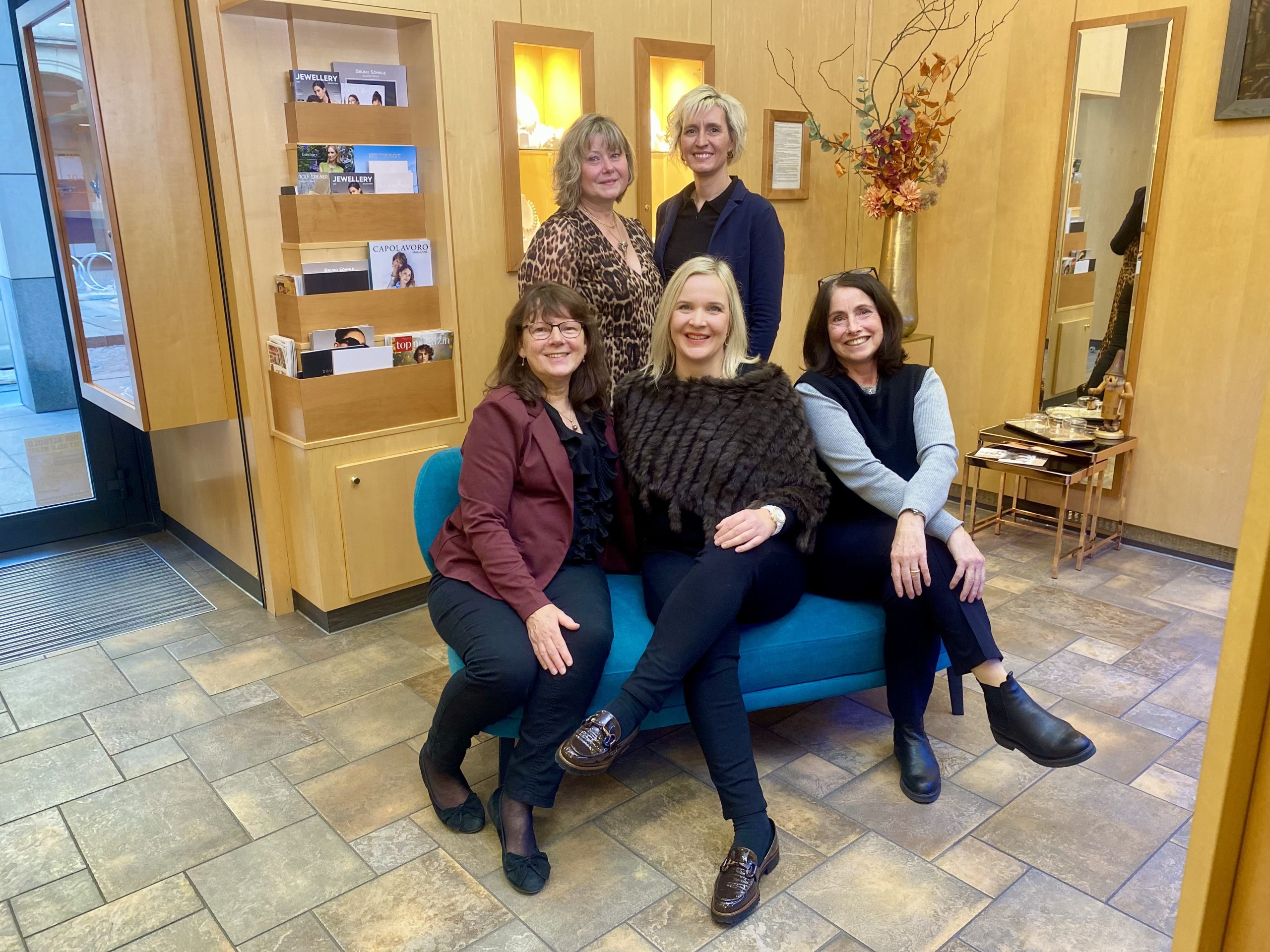 Vier Mitarbeiterinnen von Fischer Trauringe in modernem Showroom mit Holzoptik und Schmuckmagazinen im Hintergrund