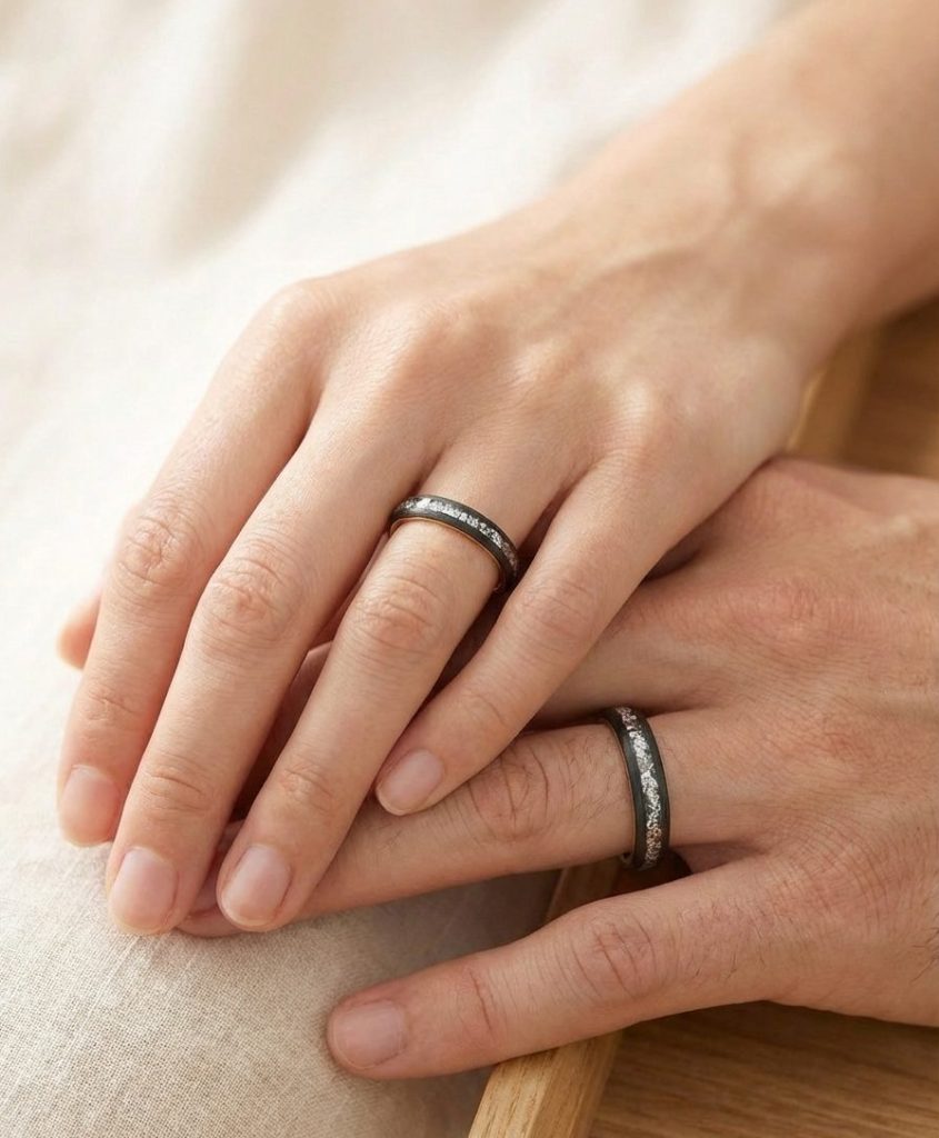 Zwei Eheringe aus Carbon mit Silver Flakes an den Fingern eines Paares