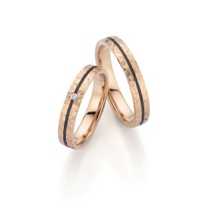Wedding rings made of apricot gold with a textured surface and black inner ring, one set with diamonds